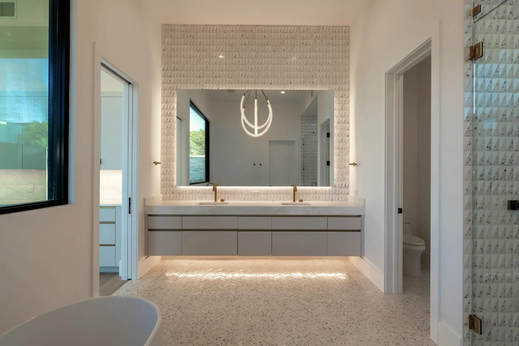 The primary bathroom: a backlit mirror set into a textured stone wall above a floating double vanity.